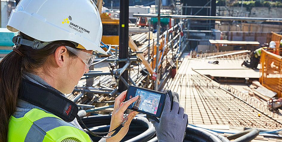 Mitarbeiterin von Smart Systems Technology zeigt an einem mobilen Gerät die Nutzung von Leica Geosystems Softwarelösungen für die digitale Baustelle.