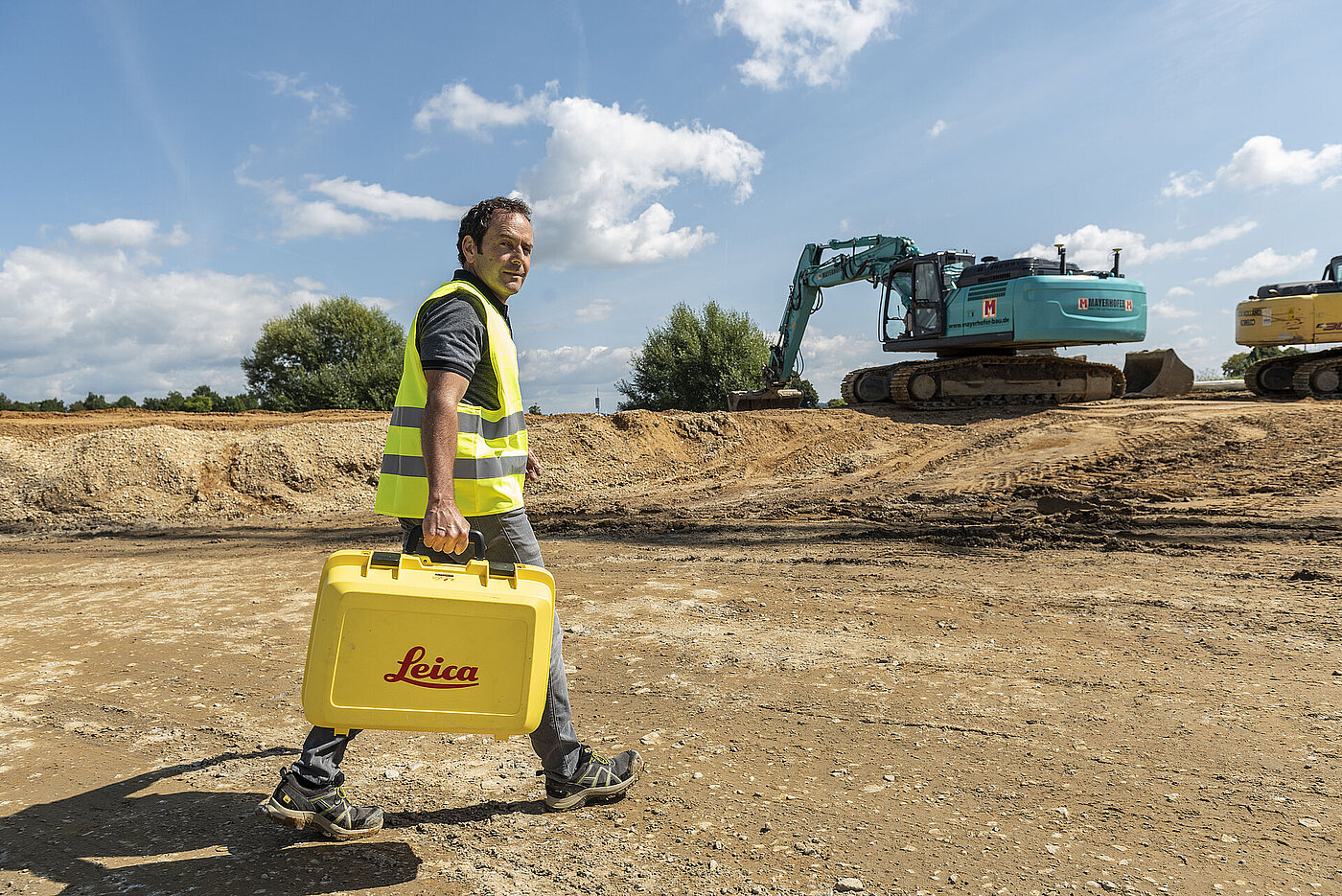 Smart Systems Mitarbeiter trägt einen Leica Koffer auf einer Baustelle