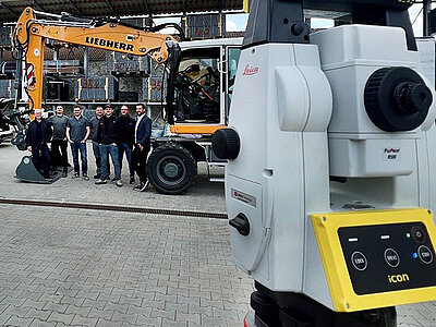 Aufnahme eines Tachymeters im Vordergrund und im Hintergrund ein G8 Liebherr Bagger und Schulungsteilnehmer