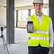 Arbeiter in Warnweste hält ein BLK 3D in die Kamera. Im Hintergrund zu sehen ein BLK2Go Gerät