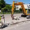 Straßenbau mit Raupenbagger und Arbeiter der mit GNSS-Rover iCG160 die Baustelle vermisst