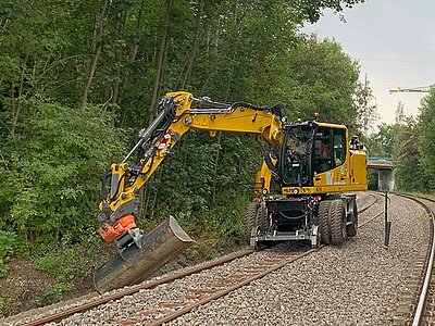 Zweiwegebagger mit Maschinensteuerung arbeitet an einer Gleisböschung sich entlang