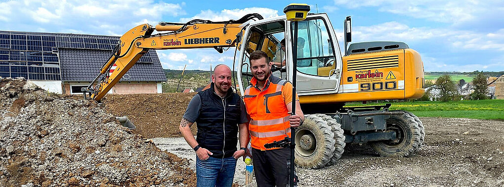Roverstab und Totalstation im Hintergrund ein Liebherr 900 Mobilbagger