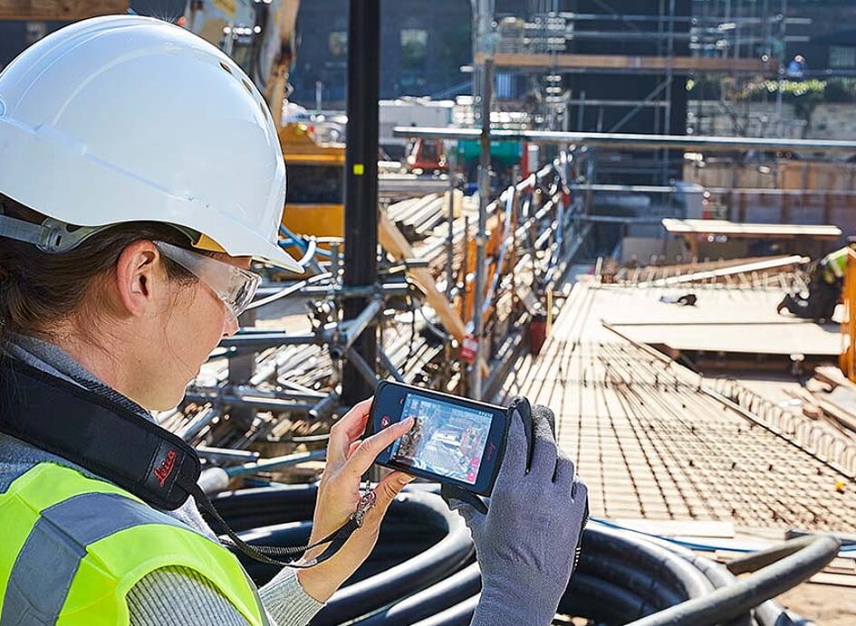 Arbeiterin auf Hochbaubaustelle mit einem BLK3 Vermessungsgerät von Leica in der Hand.