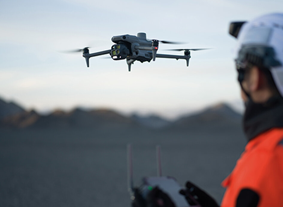 Im Vordergrund ein Mensch der eine DJI M4E Drone, die im Hintergrund zu sehen ist steuert