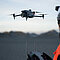 Im Vordergrund ein Mensch der eine DJI M4E Drone, die im Hintergrund zu sehen ist steuert