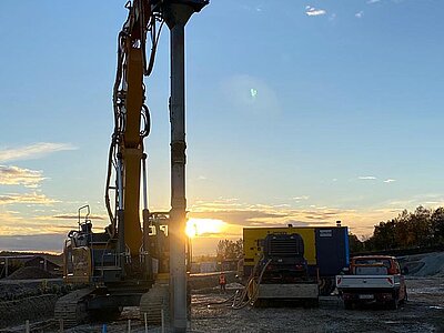 Im Sonnenuntergang auf einer Baustelle sieht man die Silhouette eines Baggers für Rüttelstopfverdichtung