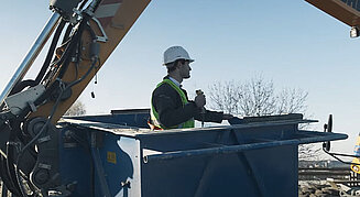 Bagger hält Arbeitskorb mit Arbeiter auf einer Baustelle in Position