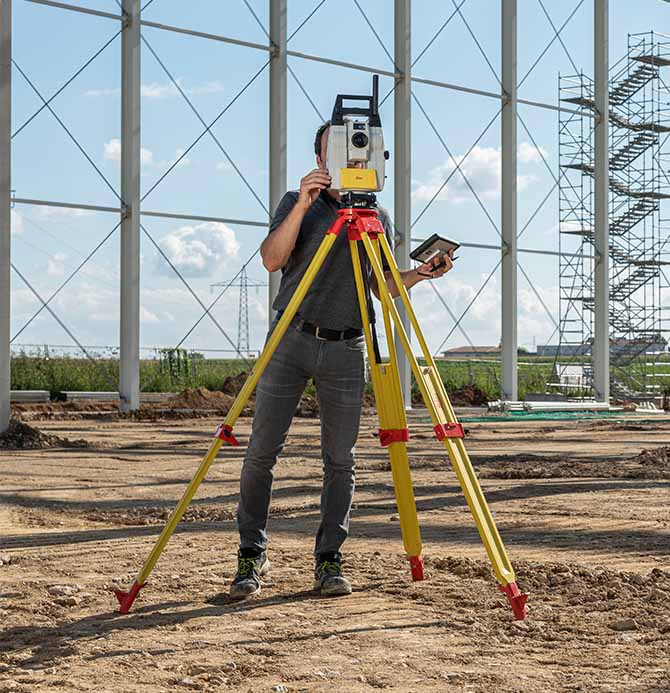 Auf offener Fläche im Hintergrund ein Gerüst - Verwendung Tachymeter als Vermessungsinstrument. Gezeigt in der Smart Systems Technology Schulung.